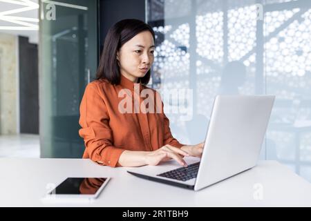 Junge asiatische Programmiererin, Entwicklerin und Tester sind fokussiert und arbeiten ernsthaft im Büro an einem Laptop. Stockfoto