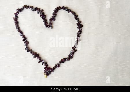 Herz zum Valentinstag bestehend aus wunderschönen weiblichen Perlen, Halsketten aus braunen dunklen Steinen, Bernstein vor einem Hintergrund aus beigefarbenem Stoff und Platz für Tex Stockfoto
