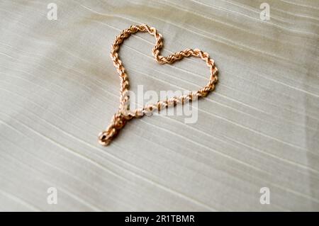 Herz aus einer Goldkette. Leuchtendes, glänzendes, glamouröses, modisches, teures Herz aus Schmuck auf beigefarbenem Hintergrund. Stockfoto