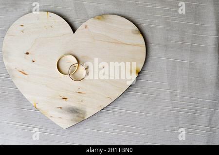 Goldene Eheringe auf einem hölzernen Herz. Leuchtende, glitzernde, glamouröse, modische, teure Herzen aus Holz mit Verzierungen für den Valentinstag Stockfoto