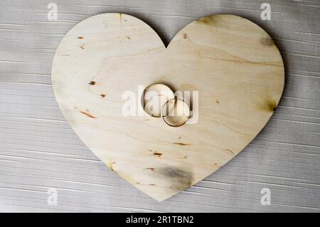 Goldene Eheringe auf einem hölzernen Herz. Leuchtende, glitzernde, glamouröse, modische, teure Herzen aus Holz mit Verzierungen für den Valentinstag Stockfoto