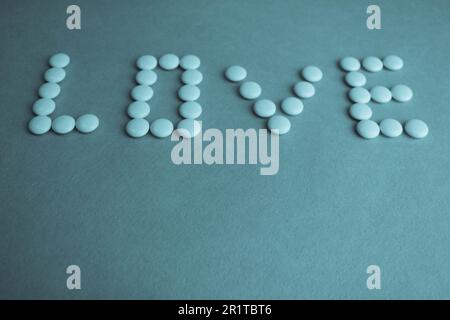 Wunderschöne Inschrift Liebe gemacht aus weißen runden glatten medizinischen Pillen, Vitaminen, Antibiotika und Kopierraum auf hellblauem Hintergrund. Flach verlegt. Stockfoto