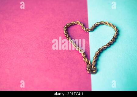 Textur einer wunderschönen goldenen festlichen Kette, einzigartiges Weben in Form eines Herzens auf pinkfarbenem lila blauem Hintergrund und Kopierbereich. Konzept: Liebe, mar Stockfoto