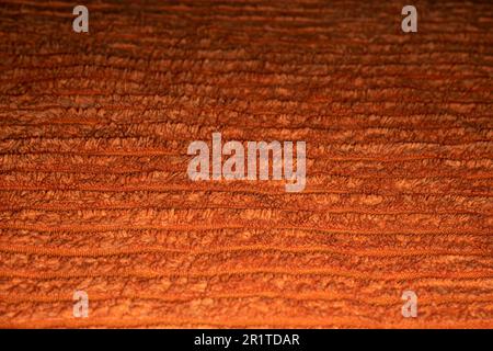 Nahaufnahme des feuchten orangefarbenen strukturierten Stoffes mit Linien zwischen dem niedrigen und dem hohen Flor des Stoffes. Weich, bequem, warm, lebendig, fröhlich, gemütlich. Backg Stockfoto