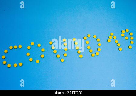 Gelbe volumetrische Tabletten sind auf einem blauen Hintergrund in Form der Aufschrift Coronavirus 2019 angeordnet. Die Medikamente sind auf einem Papierrücken angeordnet Stockfoto