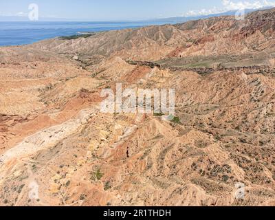 Aus der Vogelperspektive bietet sich ein Blick auf die erodierte Landschaft des Skazka Canyon in Kirgisistan mit dem Issyk-Kul-See im Hintergrund. Stockfoto