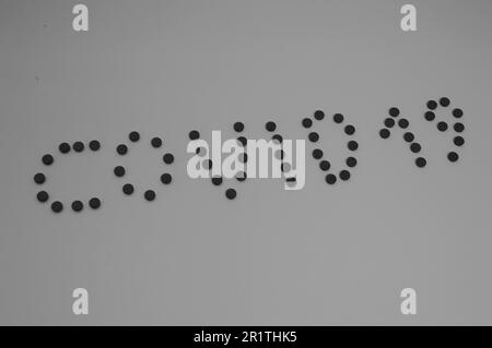 Schwarz-weiße Kovid -19-Inschrift aus runden gelben medizinischen pharmazeutischen Tabletten aus Coronavirus zur Behandlung von Pandemiekrankheiten und Stockfoto