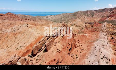 Luftaufnahme der erodierten roten Felsen von Skazka, oder Fairy Tale Canyon, in Kirgisistan mit dem Issyk-Kul-See im Hintergrund. Stockfoto