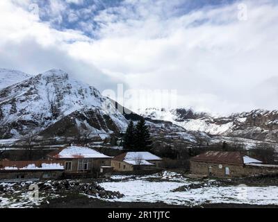 Kleine Steinhäuser, Gebäude im Dorf in einem wunderschönen bergigen kalten Winterresort mit hohen Berggipfeln, Nebel und schneebedeckten Felsen für Schneefall Stockfoto