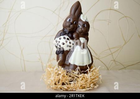 Zwei Schokoladenkaninchen. Zwei leckere, umschließende Schokoladenhasen, ein liebevolles Paar auf hellem beigefarbenem Hintergrund. Stockfoto