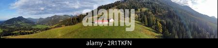 Ein Panoramablick auf ein kleines Haus auf einem üppig grünen Grasfeld mit einer majestätischen Bergkette im Hintergrund Stockfoto