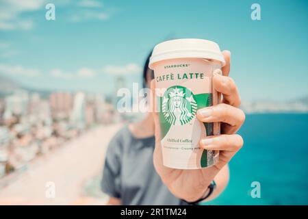 Frau hält Starbucks Kaffeetasse im Freien. Starbucks Caffe Latte gekühlter Kaffee zum Mitnehmen. Benidorm, Spanien - 15. Mai 2023 Stockfoto