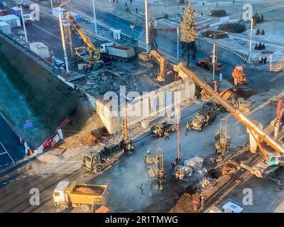 Bau einer gebrochenen Brücke an einer verkehrsreichen Straße. Straßenreparaturen, gelbe Kipplaster transportieren Asphalt, Sand für die Straßenbefestigung. Stockfoto