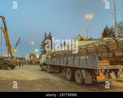 Bau einer gebrochenen Brücke an einer verkehrsreichen Straße. Ein schwerer Lkw brachte einen Metallrahmen für die Brücke auf die Baustelle. Stockfoto