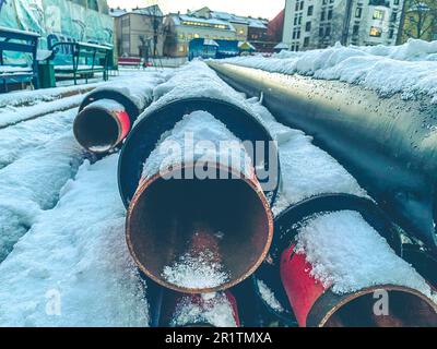 Lange, schwarze, schmale Rohre für die Verlegung von Leitungen. Metallrohre sind mit einer Schneeschicht bedeckt. Abwasserentsorgung. Renovierungsarbeiten in einem Wohnhaus Stockfoto