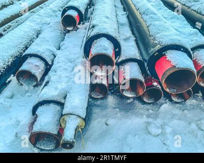 Material für Reparaturarbeiten. Abwasserrohre zur Verlegung von Kommunikationsleitungen in Wohngebieten. Lange, schwarze Polypropylenrohre. Rohre liegen auf weißem Schnee. Stockfoto