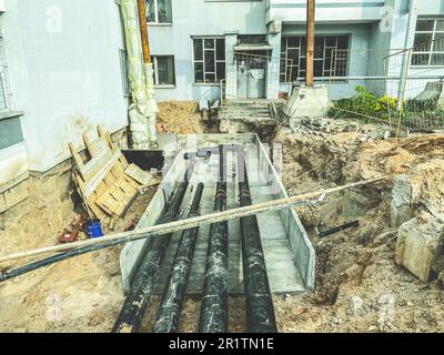 Schwarze, lange Rohre aus Polypropylen werden für die Kommunikation unterirdisch verlegt. Verlegung von Rohren für die Sanierung von Wohngebäuden. Stockfoto