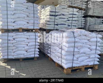 Große Beutel aus weißem Polypropylen mit Baumaterialien oder Schüttgut liegen auf Holzpaletten in einem Industrielager übereinander. Stockfoto