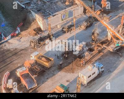 Bau einer neuen Überführung im Stadtzentrum auf einer verschneiten Straße. Straßenreparaturen, gelbe Kipplaster transportieren Asphalt, Sand für die Straßenbefestigung. Stockfoto