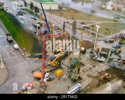 Blick aus der Höhe einer großen Baustelle. Bau einer Überführung im Stadtzentrum während des Regens. Baumaschinen vor Ort und cr Stockfoto