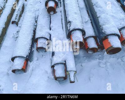 Material für Reparaturarbeiten. Abwasserrohre zur Verlegung von Kommunikationsleitungen. Lange, schwarze Polypropylenrohre. Die Rohre liegen auf weißem Schnee und warten darauf, dass sie im Garten liegen Stockfoto