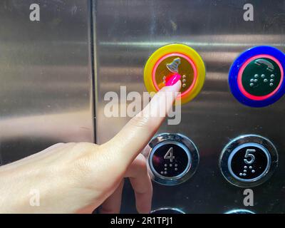 Der gepflegte Finger einer Frau an der Hand drückt einen Knopf in einem modernen, wunderschönen Aufzug in einem Hochhaus. Stockfoto