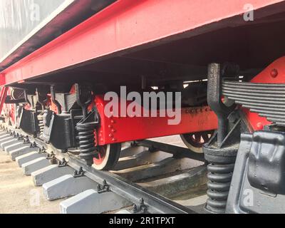 Große Eisenräder eines rot-schwarzen Zuges, der auf Schienen und Aufhängungselementen steht, mit Federn einer alten industriellen Dampflokomotive. Stockfoto
