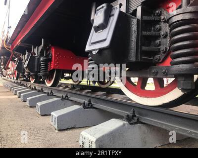 Große Eisenräder eines rot-schwarzen Zuges, der auf Schienen und Aufhängungselementen steht, mit Federn einer alten industriellen Dampflokomotive. Stockfoto