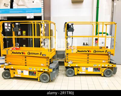 Großer gelber mobiler hydraulischer Aufzug auf Rädern zum Heben und Bewegen von Personen und Fracht in Regalen in einem Supermarkt im Lager. Weißrussland, Minsk, Octob Stockfoto