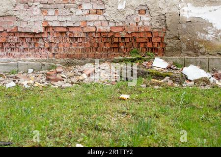 Einstürzende Wand aufgrund von Wassereintritt, verschlissene rote Ziegelwand und grünes Gras Stockfoto