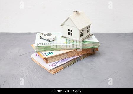 Miniaturmodell Haus und Auto auf Stapeln mit 50-, 100- und 500-Euro-Banknoten. Stockfoto