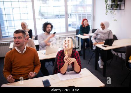 Multiethnische Studenten, die sich über den Dozenten in einem Klassenzimmer hinter seinem Rücken lustig machen. Intelligente junge Menschen studieren an einer Hochschule. Stockfoto