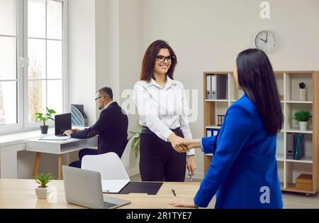 Zwei fröhliche Geschäftsfrauen, die sich in einem modernen Büro die Hand schütteln Stockfoto