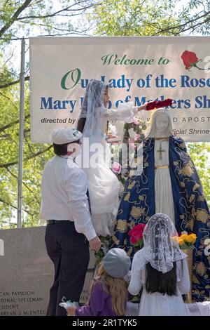 Ein 8 Jahre altes spanisches Mädchen aus Corona führt die römisch-katholische Zeremonie der Maikrönung durch. Vor der Krone legt sie Blumen auf die Statue von Mary. Stockfoto