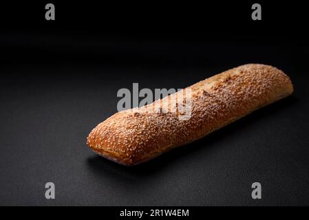 Knuspriges Weizenmehl-Baguette mit Sesamsamen auf einem Holzbrett auf dunklem Betonhintergrund Stockfoto