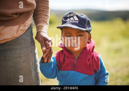 Tsiafahy, Madagaskar - 25. April 2019: Unbekannter junger madagassischer Junge in Fleecejacke und Baseballmütze, hält ihre Mutterhand, Nahaufnahme Porträt - Menschen Stockfoto