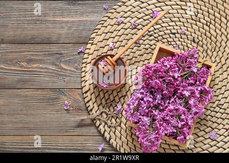 Korbmatte und Schachtel mit wunderschönen Fliederblumen mit Honig auf braunem Holzhintergrund Stockfoto