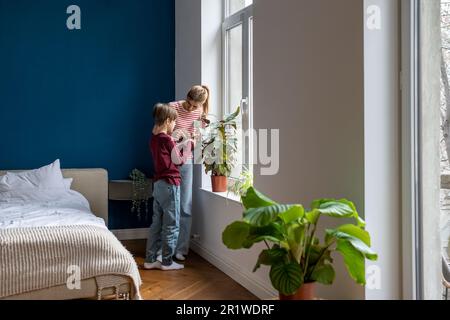 Mutter, die dem Sohn beibringt, wie man Pflanzen pflegt. Mutter erklärt dem Kind die Photosynthese. Pflanzenliebhaber. Stockfoto