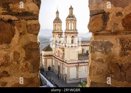 Die Kirche Maria Maria der Inkarnation, die durch die Stadtmauern der Burg Olvera in der Stadt Pueblo Blanco in Olvera, Spanien, besichtigt wurde. Die Pfarrkirche wurde 1822 erbaut, aber die Burg wurde im 12. Jahrhundert von arabischen Herrschern auf einem Fundament erbaut, das die Römer im 3. Jahrhundert hinterließen. Stockfoto