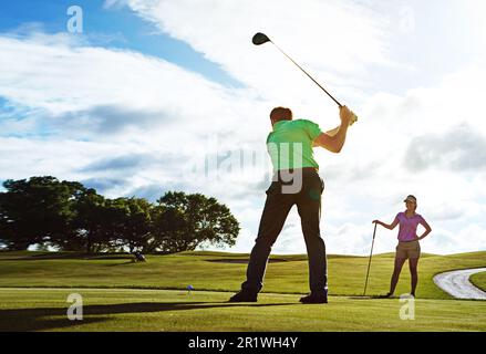 Er arbeitet an seinem Schwung mit seinem Partner. Ein Paar, das zusammen Golf auf einem Fairway spielt. Stockfoto