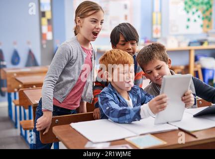 Wer kann das albernste Gesicht machen? Grundschulkinder mit einem Tablet im Unterricht. Stockfoto