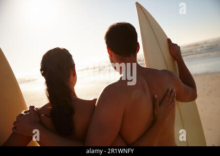 Liebe zusammen, Surfen zusammen. Rückblick auf ein junges Surferpaar mit Blick auf den Strand und die weit entfernten Wellen. Stockfoto