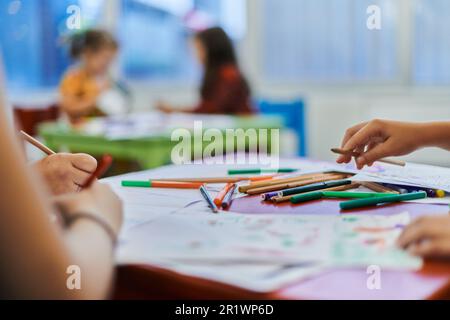 Nahaufnahme von Kindern während eines Kunstunterrichts in einer Kindertagesstätte oder Zeichnung in der Grundschule mit einer Lehrerin. Stockfoto