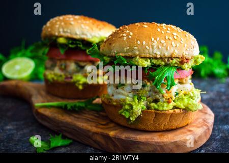 Shrimp Burger mit Cilantro und Guacamole auf Sesamsamen Brötchen: Hamburger mit Meeresfrüchten, garniert mit Guacamole und Tomatenscheiben Stockfoto