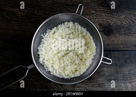 Aufgetauter gefrorener Blumenkohl-Reis in einem Sieb: Reiskohl in einem Sieb, das über einer Mischschüssel platziert wird Stockfoto