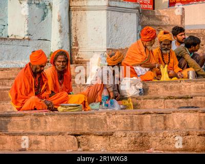 Varanasi, Indien - 13. November 2015. Hindu-Männer in traditioneller safranfarbener Sadhu-Kleidung sitzen auf Ghats in der Nähe des Ganges mit Spendenschüsseln. Stockfoto
