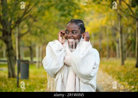 Afrikanische Frau lächelt und hört im Herbst Musik. Stockfoto