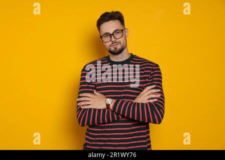 Ein gutaussehender Mann in gestreiftem Sweatshirt und Brille auf gelbem Hintergrund Stockfoto