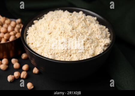 Kichererbsenmehl in Schüssel und Samen auf schwarzem Tisch Stockfoto