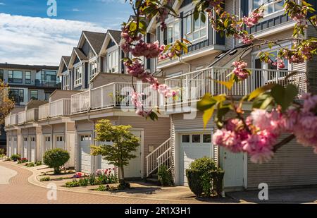 Fassade neuer Wohngemeindenhäuser. Moderne Gebäude mit Garagen in Richmond, Kanada. Moderner Apartmentkomplex im Frühjahr. Konzept des Harnstoffs Stockfoto